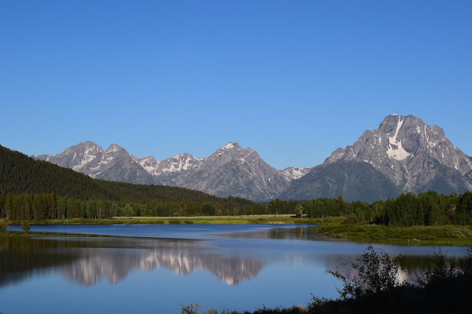 A photo of the Grand Tetons and a lake, with a reflection of the mountains in the water.